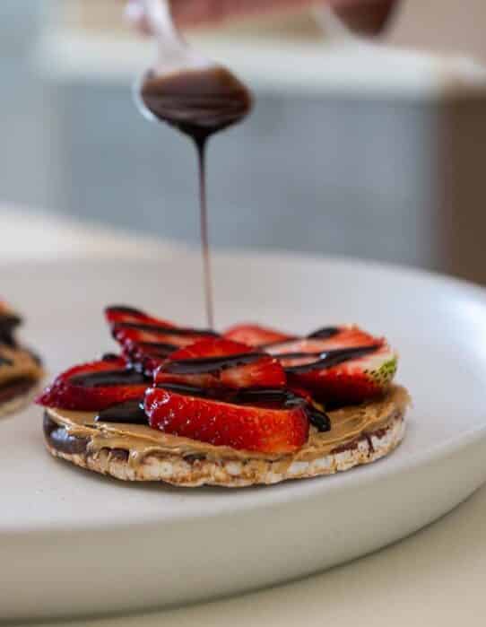 Galleta de arroz cubierta con chocolate con topping de mantequilla de maní, fresas y chocolate líquido